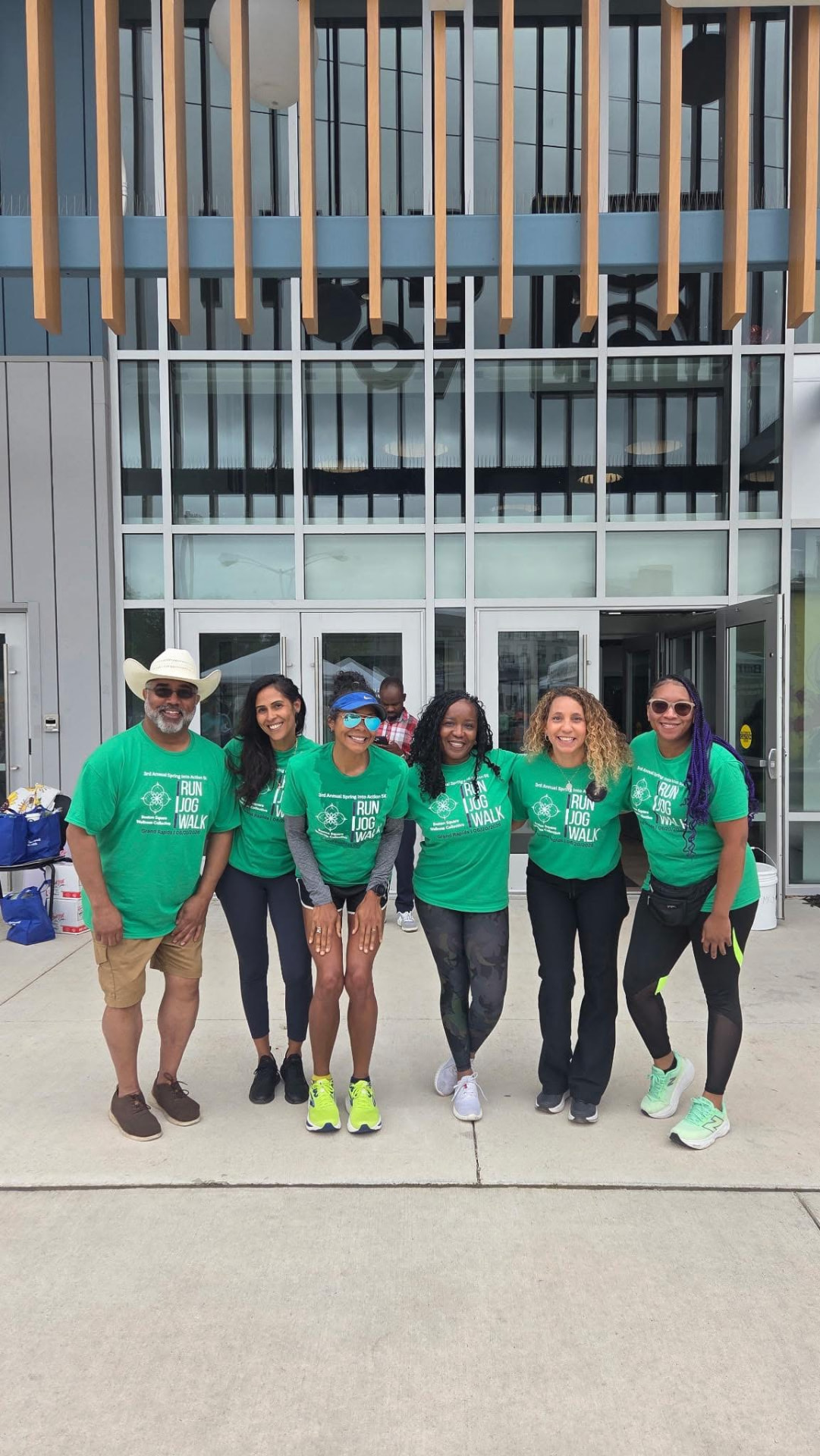 Six community members in matching green Spring Into Action 5K t-shirts posing together outside the event entrance
